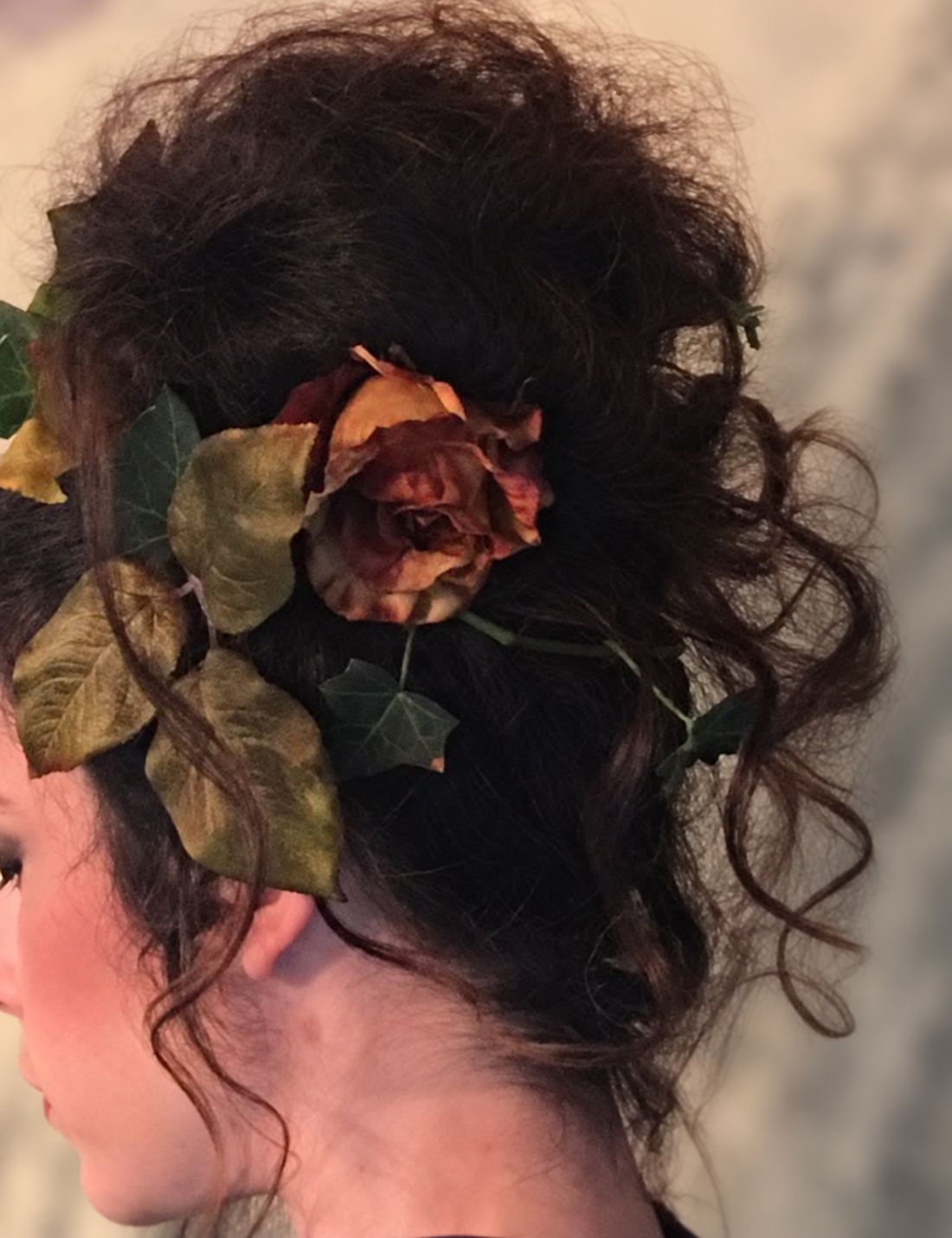 Dark hair swept into an updo with a rose and leafy accents, styled by Kellie
